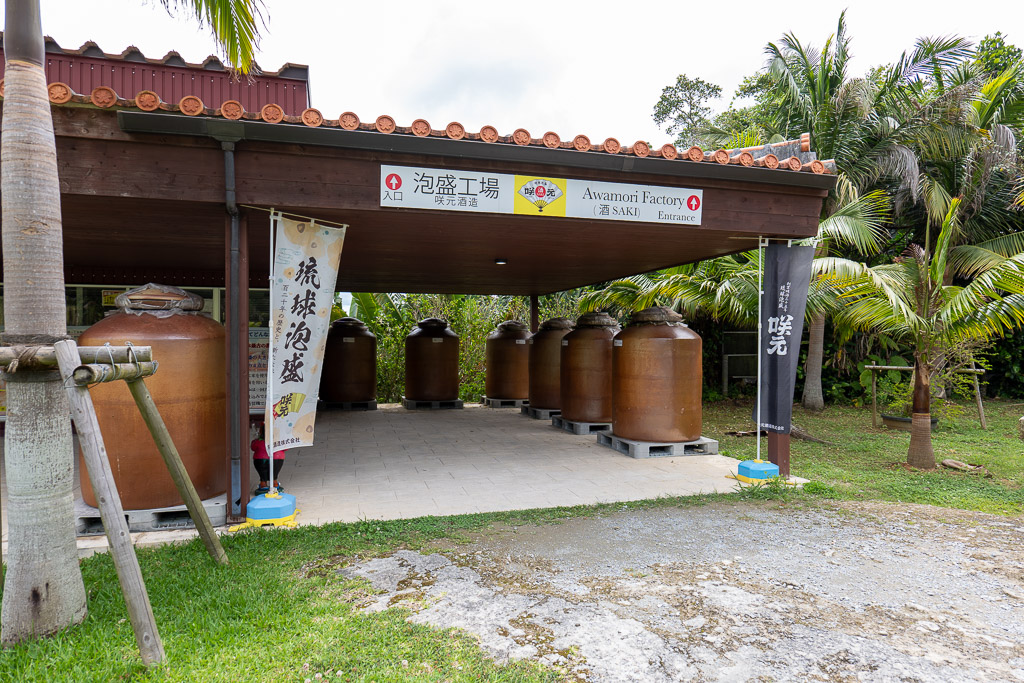 咲元酒造泡盛工場入口 — 七個巨大紅褐色泡盛甕並排與琉球泡盛旗