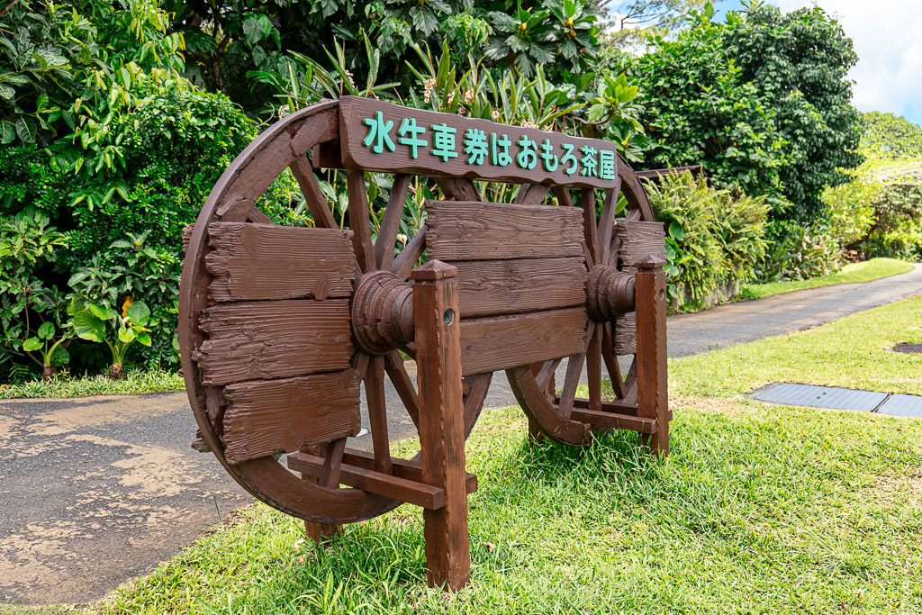 BIOS之丘水牛車購票指示牌 — 巨大木製車輪上寫著水牛車票券於おもろ茶屋販售
