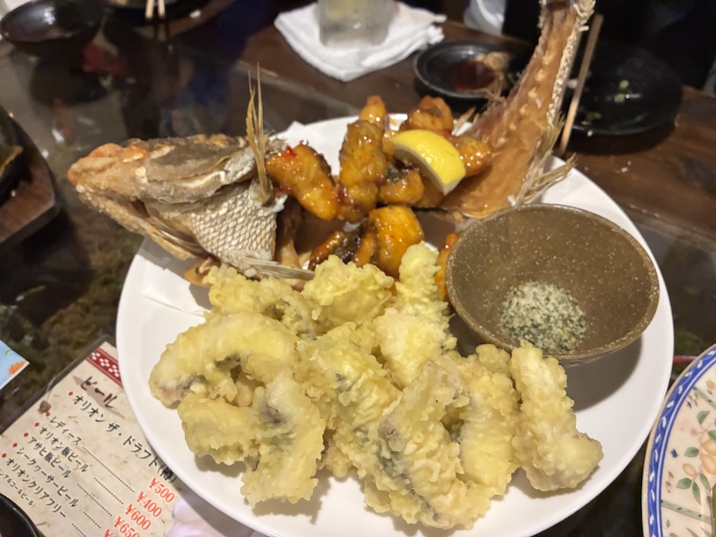 沖繩居酒屋整尾炸魚配天婦羅，旁邊有手寫日文飲料菜單——日本eSIM協助即時翻譯點餐