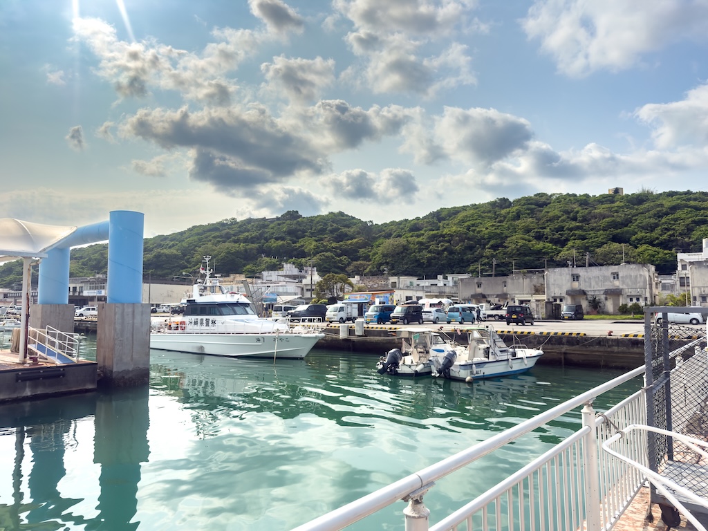 沖繩水納島浮潛 — 渡久地港停靠的快艇與晴朗夏日天空
