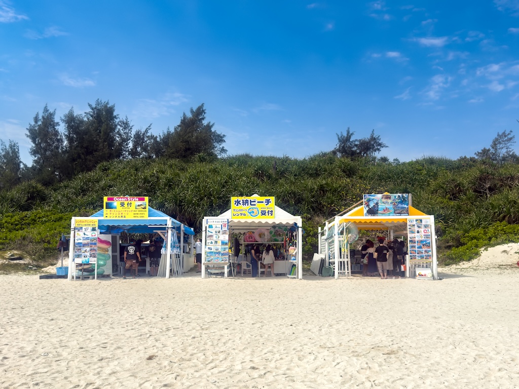 水納島海灘上的浮潛接待處帳篷 — 沙灘、藍天與沿岸排列的活動帳篷
