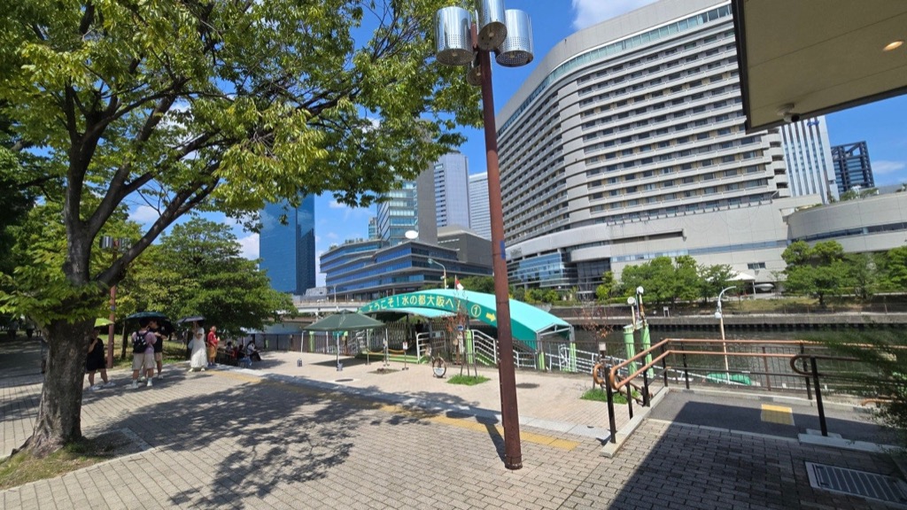 9月上旬的大阪中之島,遊客撐著陽傘走在強烈陽光下的河濱步道